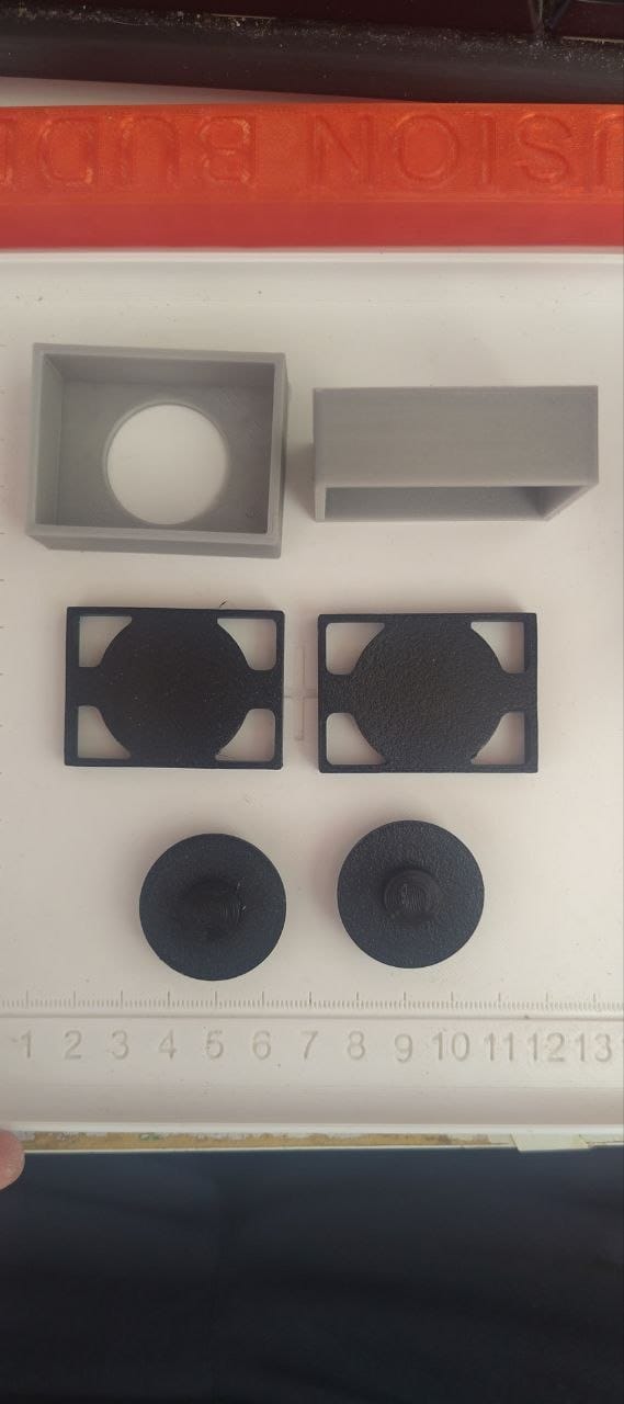 All the 3D printed parts laid out before assembly: the USB-C housing (gray), the chip package cover (gray), two button frames (black), and two button caps (black).